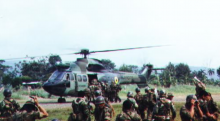 A helicopter in the middle of the grass, with surrounding soldiers. Image is taken from 1995 Cenepa War.
