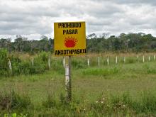 A yellow warning sign says "Prohibited to pass" in Spanish and the local language, is placed in a green field.